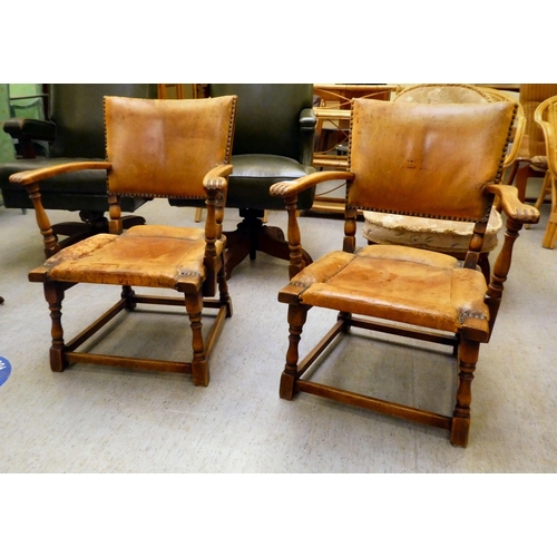 190 - A pair of 1930w oak framed chairs with brown hide upholstered backs and seats, raised on block legs