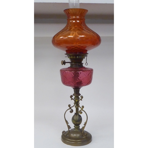 107 - A reproduction of a Victorian style brass oil lamp with a cranberry coloured glass reservoir and an ... 