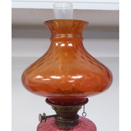 107 - A reproduction of a Victorian style brass oil lamp with a cranberry coloured glass reservoir and an ... 