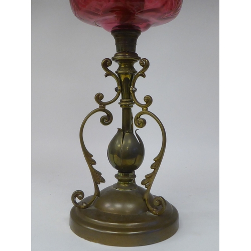 107 - A reproduction of a Victorian style brass oil lamp with a cranberry coloured glass reservoir and an ... 