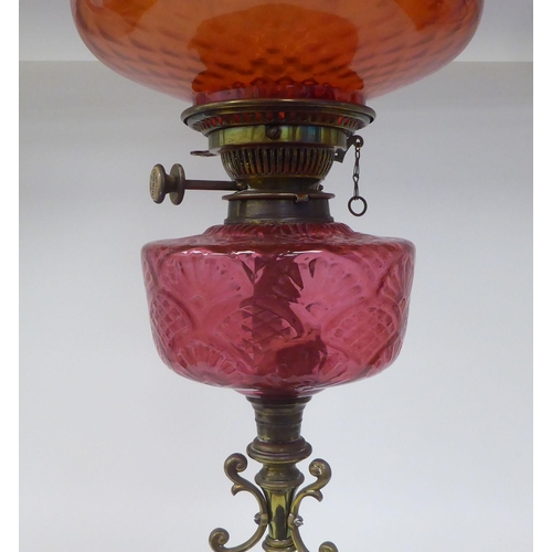 107 - A reproduction of a Victorian style brass oil lamp with a cranberry coloured glass reservoir and an ... 