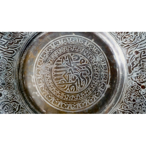 63 - A late 19thC Middle Eastern bi-coloured copper charger with opposing iron loop handles, engraved wit... 