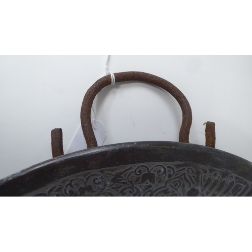 63 - A late 19thC Middle Eastern bi-coloured copper charger with opposing iron loop handles, engraved wit... 