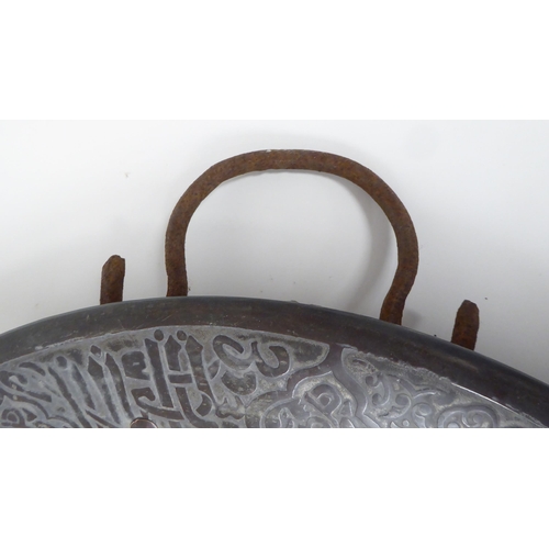 63 - A late 19thC Middle Eastern bi-coloured copper charger with opposing iron loop handles, engraved wit... 