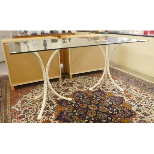 15 - A modern table, the plate glass top on two cream painted bamboo effect, cast metal tripods  29