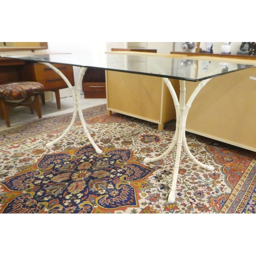 15 - A modern table, the plate glass top on two cream painted bamboo effect, cast metal tripods  29
