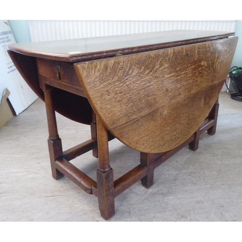 123 - An 18th/19thC style rustic oak drop-leaf dining table with an end drawer, the oval top raised on tur... 