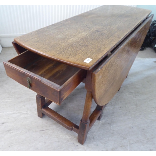 123 - An 18th/19thC style rustic oak drop-leaf dining table with an end drawer, the oval top raised on tur... 