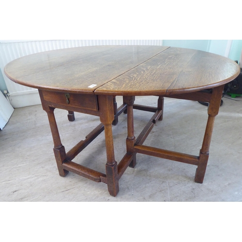 123 - An 18th/19thC style rustic oak drop-leaf dining table with an end drawer, the oval top raised on tur... 