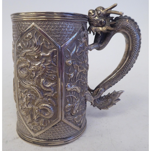 129 - A late 19thC Chinese silver coloured metal mug of tapered cylindrical form with a cast S-shape drago... 