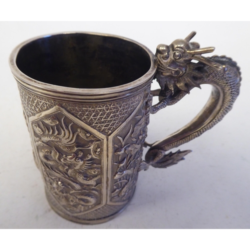 129 - A late 19thC Chinese silver coloured metal mug of tapered cylindrical form with a cast S-shape drago... 