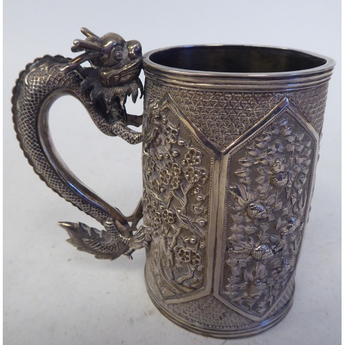 129 - A late 19thC Chinese silver coloured metal mug of tapered cylindrical form with a cast S-shape drago... 