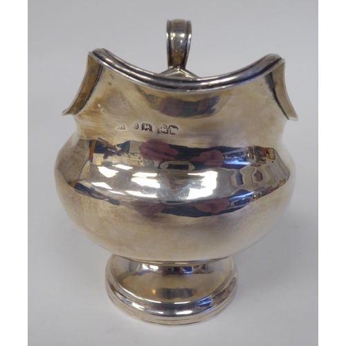 132 - A silver pedestal cream jug of squat, bulbous form with an applied wire rim and C-scrolled handles&n... 