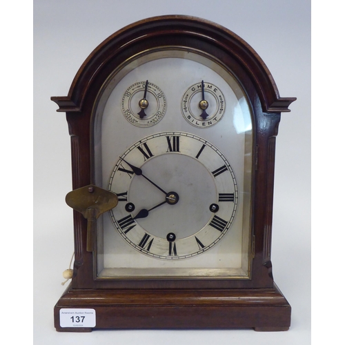 137 - A late 19th/early 20thC mahogany round arched cased mantel clock with a full-height window, on a pli... 