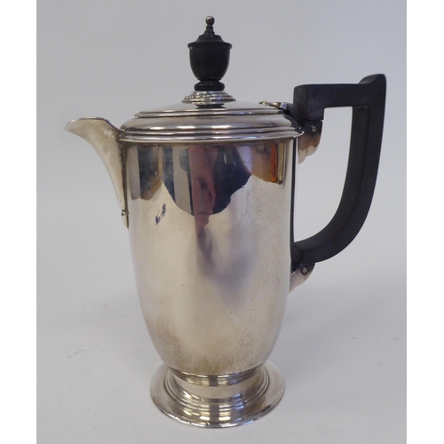 168 - A silver hot water pot of baluster form with a hinged lid, ebonised handle and knop, on a splayed fo... 