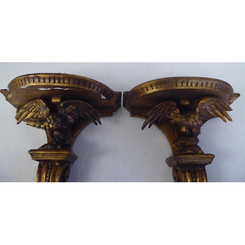 97 - A pair of late 19thC carved wooden and gilt gesso moulded wall brackets, each featuring a semi-circu... 