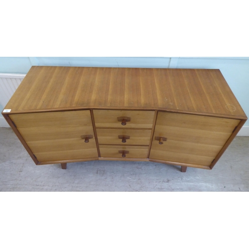 84 - A 1970s two-tone teak inverted breakfront sideboard with a bank of three central drawers, flanked by... 