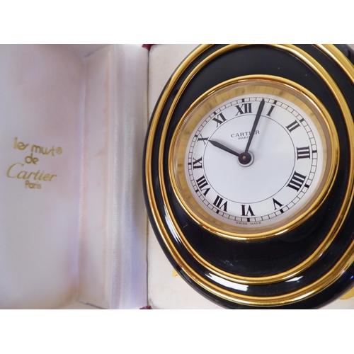 23 - A Cartier travel clock, No.7511 00638, in a gilded and black enamel oval case, on an easel stand; th... 