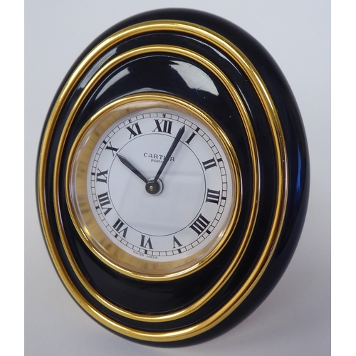 23 - A Cartier travel clock, No.7511 00638, in a gilded and black enamel oval case, on an easel stand; th... 