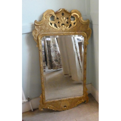 61 - An early 20thC mirror, the shaped, bevelled plate set in a gilded pine frame  44