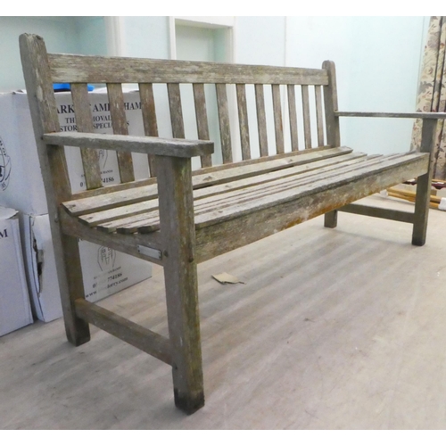 65 - A slatted weathered teak garden bench, raised on square legs  60