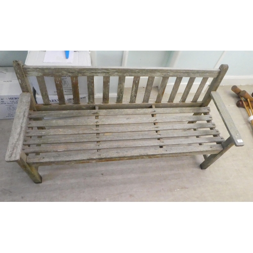 65 - A slatted weathered teak garden bench, raised on square legs  60