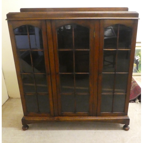 72 - A 1930s oak display cabinet with three partially glazed doors, on a plinth and bun feet  49