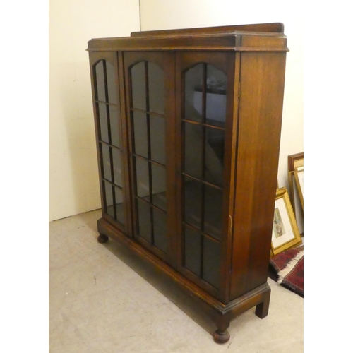 72 - A 1930s oak display cabinet with three partially glazed doors, on a plinth and bun feet  49