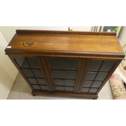 72 - A 1930s oak display cabinet with three partially glazed doors, on a plinth and bun feet  49