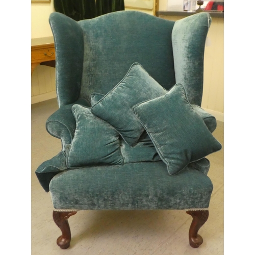130 - A 20thC Georgian style wingback chair with scrolled arms, upholstered in crushed turquoise coloured ... 