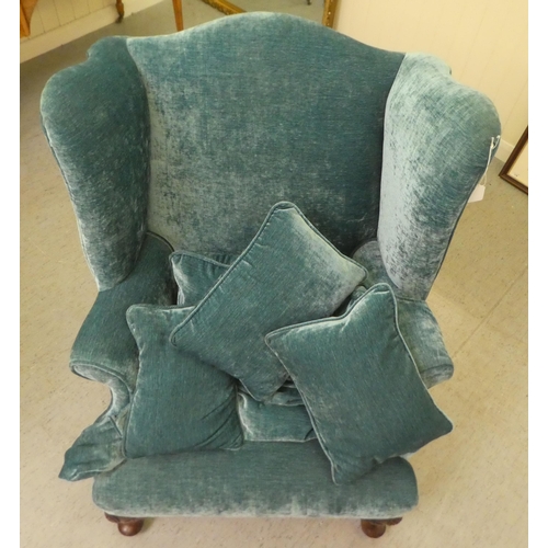 130 - A 20thC Georgian style wingback chair with scrolled arms, upholstered in crushed turquoise coloured ... 