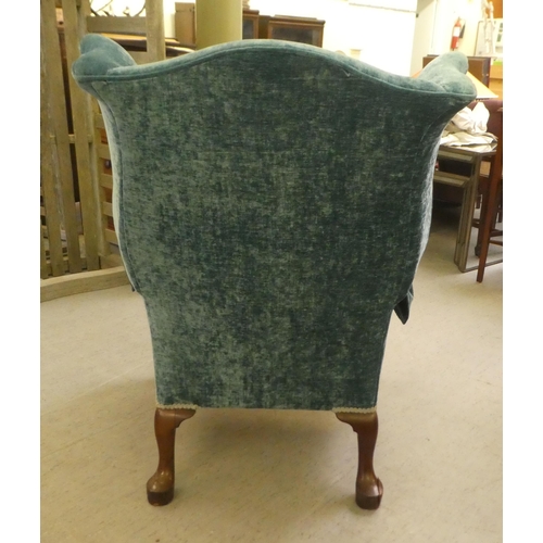 130 - A 20thC Georgian style wingback chair with scrolled arms, upholstered in crushed turquoise coloured ... 
