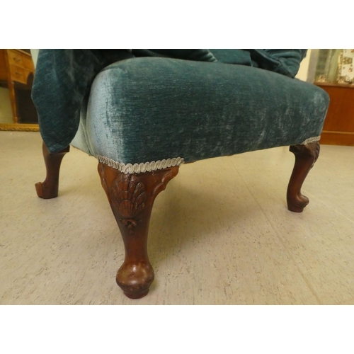 130 - A 20thC Georgian style wingback chair with scrolled arms, upholstered in crushed turquoise coloured ... 