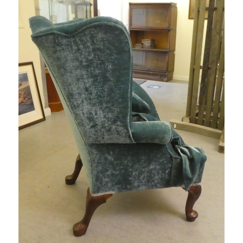 130 - A 20thC Georgian style wingback chair with scrolled arms, upholstered in crushed turquoise coloured ... 
