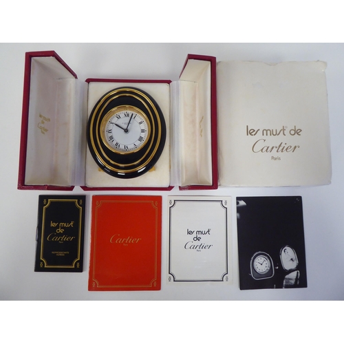 138 - A Cartier travel clock, No.7511 00638, in a gilded and black enamel oval case, on an easel stand; th... 