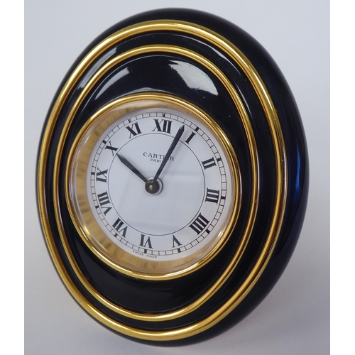 138 - A Cartier travel clock, No.7511 00638, in a gilded and black enamel oval case, on an easel stand; th... 