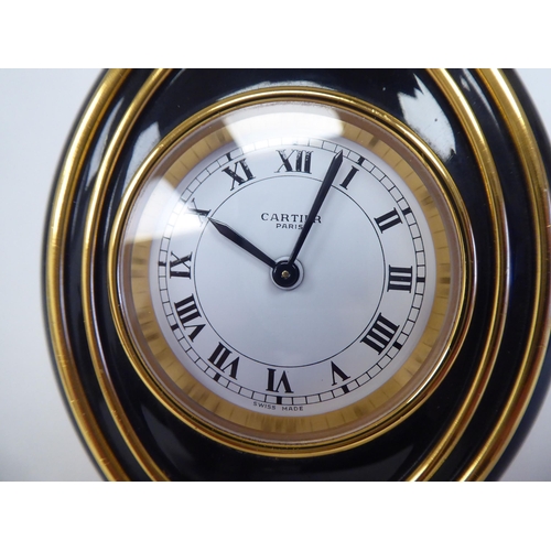 138 - A Cartier travel clock, No.7511 00638, in a gilded and black enamel oval case, on an easel stand; th... 