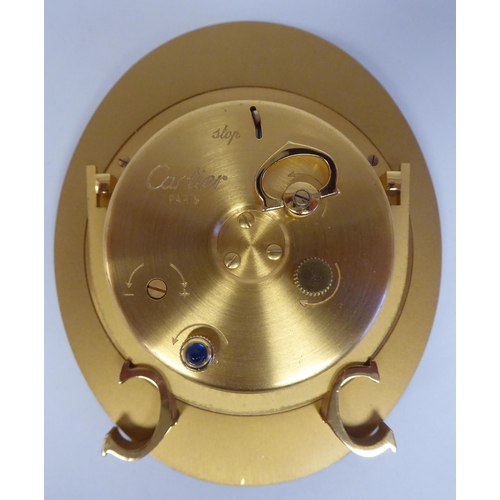 138 - A Cartier travel clock, No.7511 00638, in a gilded and black enamel oval case, on an easel stand; th... 