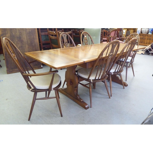 153 - An Ercol Golden Dawn beech and elm draw leaf dining table with a panelled top, raised on shaped tres... 