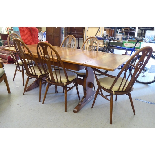153 - An Ercol Golden Dawn beech and elm draw leaf dining table with a panelled top, raised on shaped tres... 