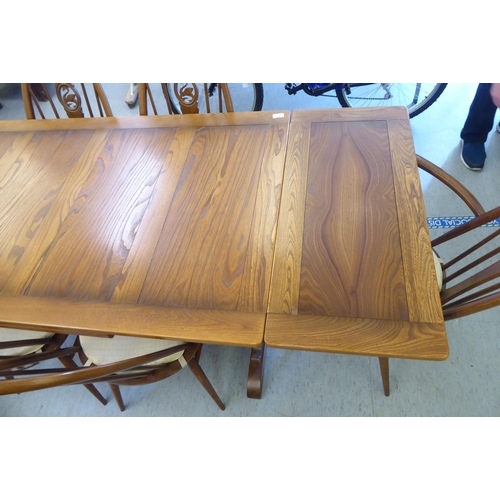 153 - An Ercol Golden Dawn beech and elm draw leaf dining table with a panelled top, raised on shaped tres... 