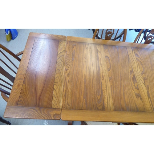 153 - An Ercol Golden Dawn beech and elm draw leaf dining table with a panelled top, raised on shaped tres... 