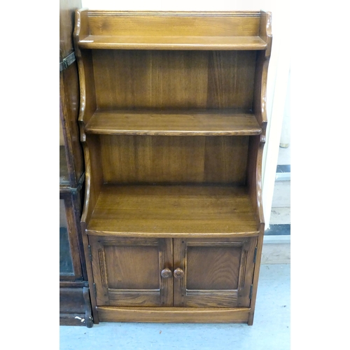 158 - An Ercol Golden Dawn beech and elm waterfall front, two tier bookcase, over a pair of panelled doors... 