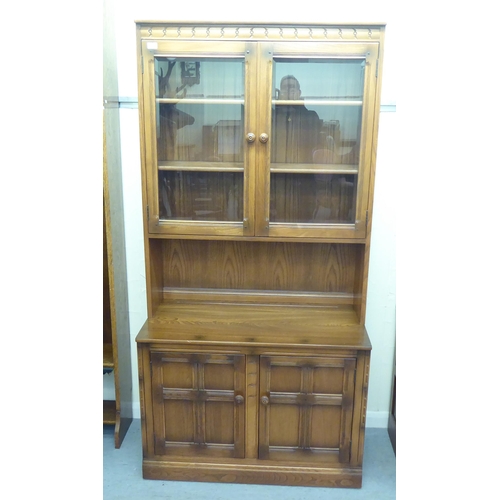 173 - An Ercol Golden Dawn beech and elm livingroom unit, the upper part enclosed by a pair of bevelled gl... 