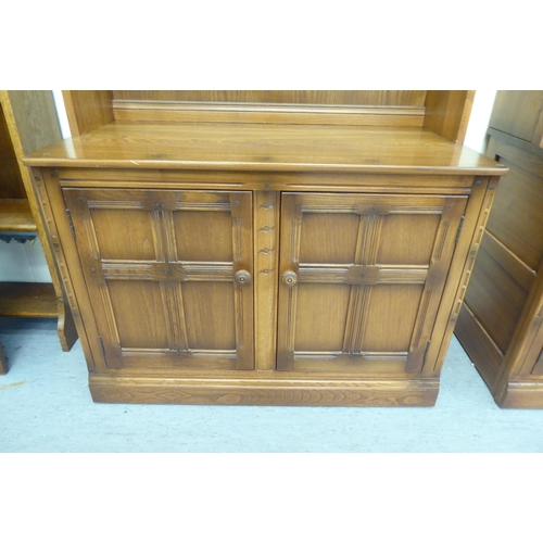 173 - An Ercol Golden Dawn beech and elm livingroom unit, the upper part enclosed by a pair of bevelled gl... 