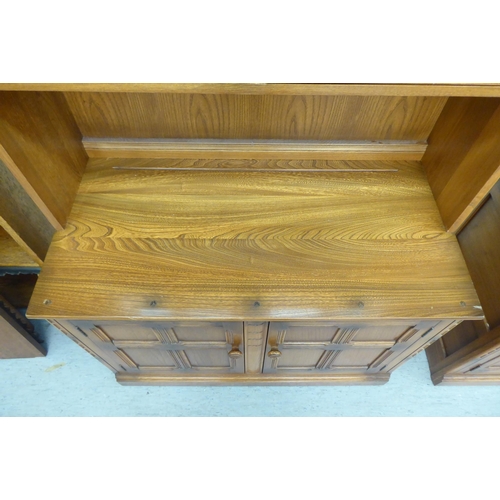 173 - An Ercol Golden Dawn beech and elm livingroom unit, the upper part enclosed by a pair of bevelled gl... 