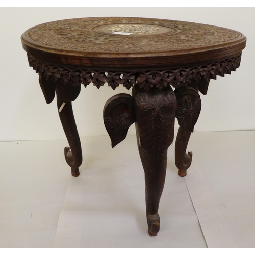 176 - An Indian carved teak side table with an inlaid bone central motif, raised on elephants' head suppor... 