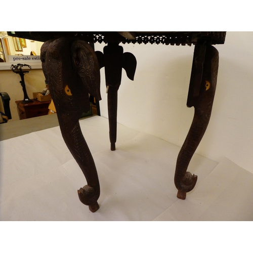 176 - An Indian carved teak side table with an inlaid bone central motif, raised on elephants' head suppor... 