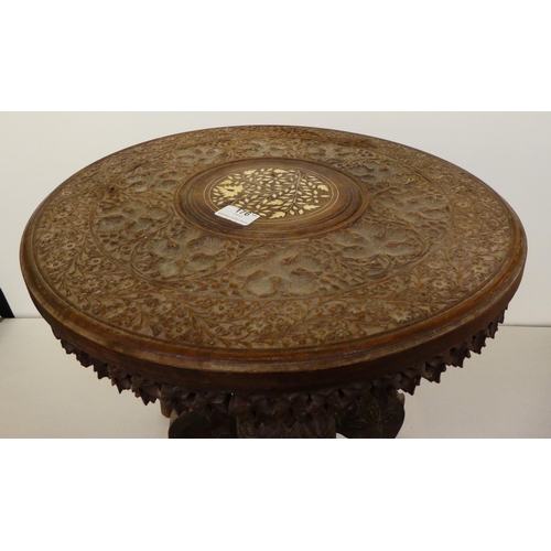176 - An Indian carved teak side table with an inlaid bone central motif, raised on elephants' head suppor... 