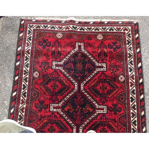 21 - A Persian rug, decorated with three central diamond shaped motifs, bordered by repeating designs, on... 